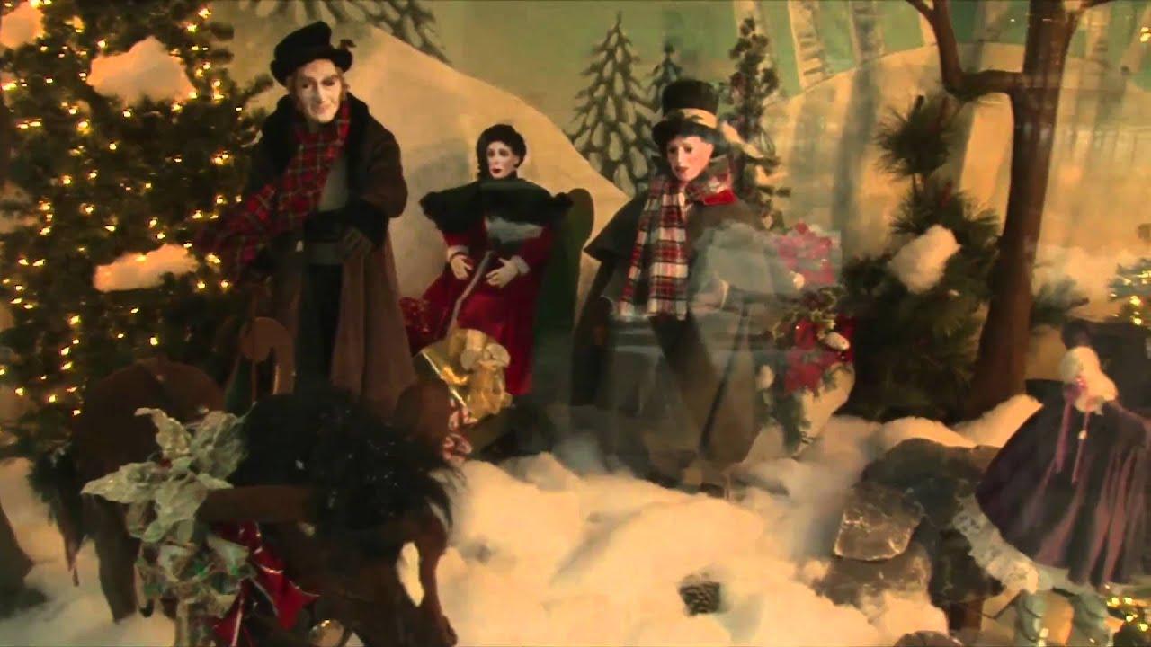 People in winter clothing pose in a festive holiday window display with trees and lights.