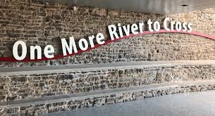 Large sign on a brick wall reading “One More River to Cross”.