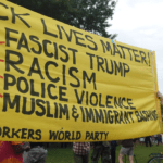 Yellow protest banner with bold black text reading “Fascist Trump,” “Racism,” and “Police violence.”