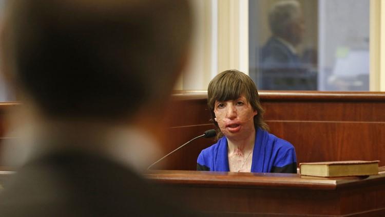 Woman in a courtroom wearing a blue top sits at a table with microphones.