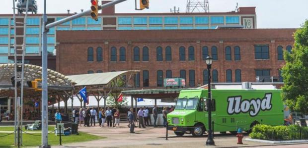 Green truck with large “Lloyd” lettering parked in front of a brick building and event crowd.