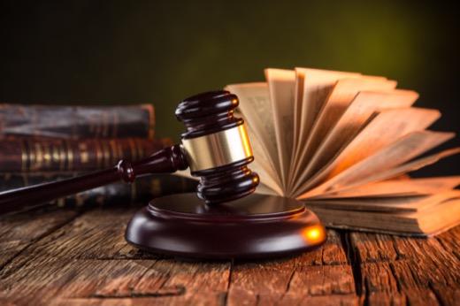 Brown gavel on a wooden table beside an open stack of law books.