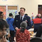 Uniformed officer stands and speaks to people seated in a room with tables.