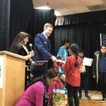Speaker in blazer hands items to children near a podium with a Western New York logo.
