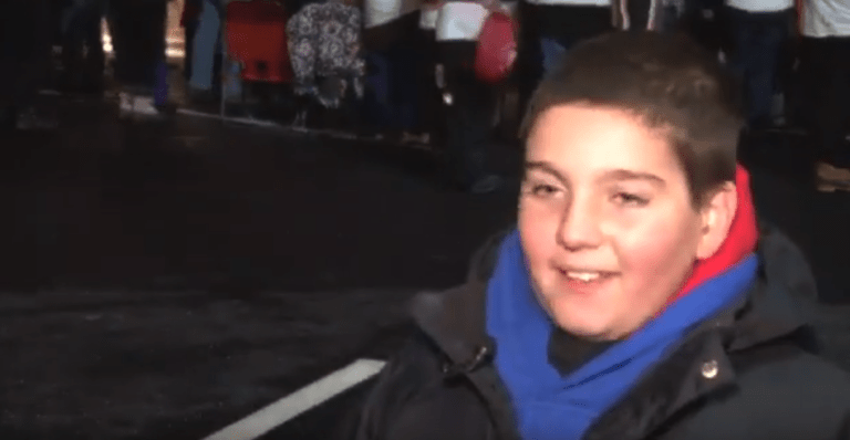 Child smiling outdoors at night wearing a blue scarf and dark winter jacket