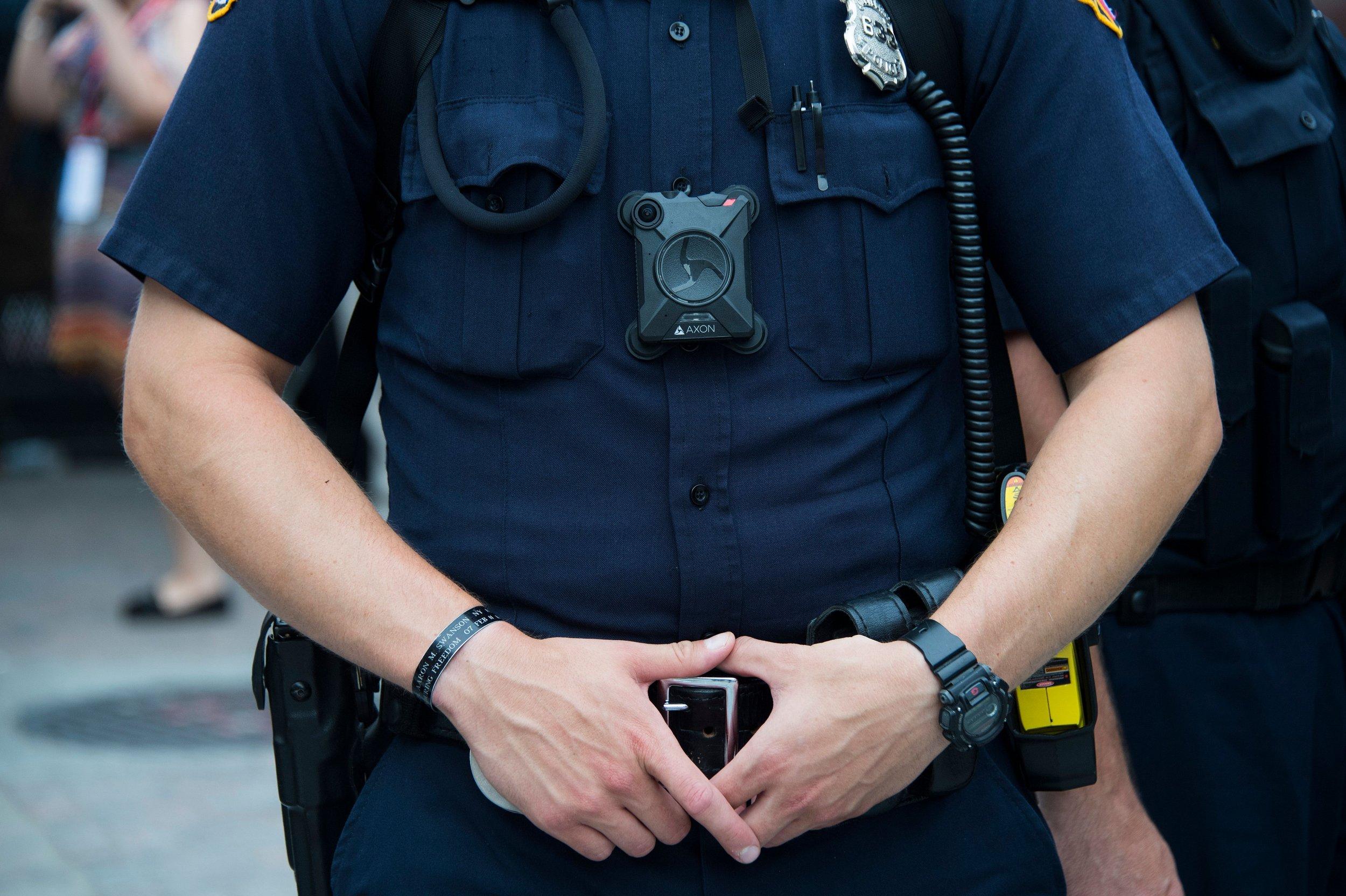 Officer in uniform wearing a body camera, holding a smartphone with both hands.