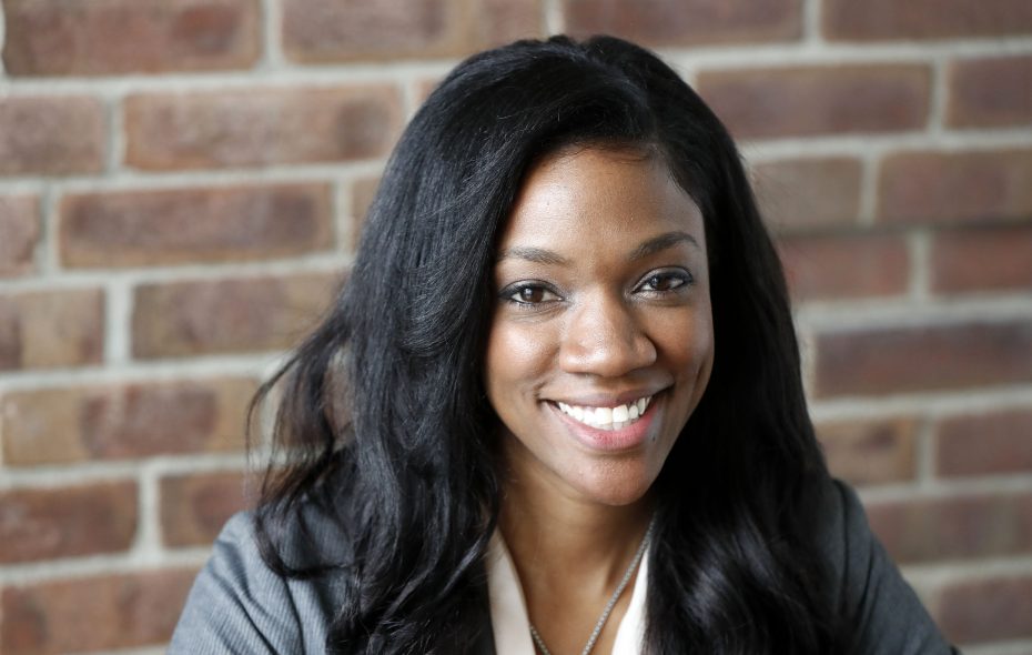 Smiling woman with long dark hair sitting in front of a brick wall background.