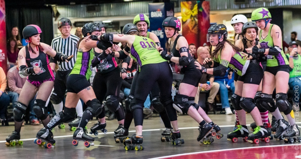 Roller derby skaters in helmets and colorful uniforms skate and jostle near the bench