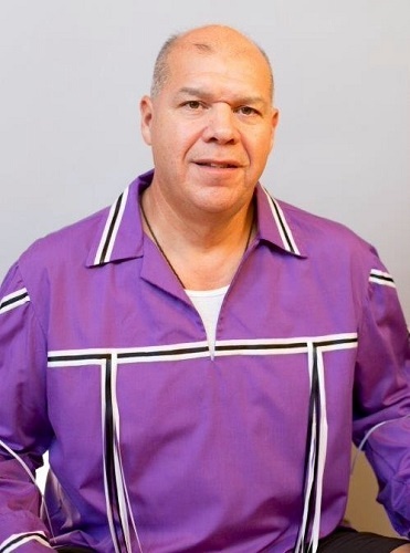 A man wearing a purple work jacket with white stripes looks at the camera.