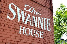 “Swannie House” sign painted on a brick wall with trees in the background.