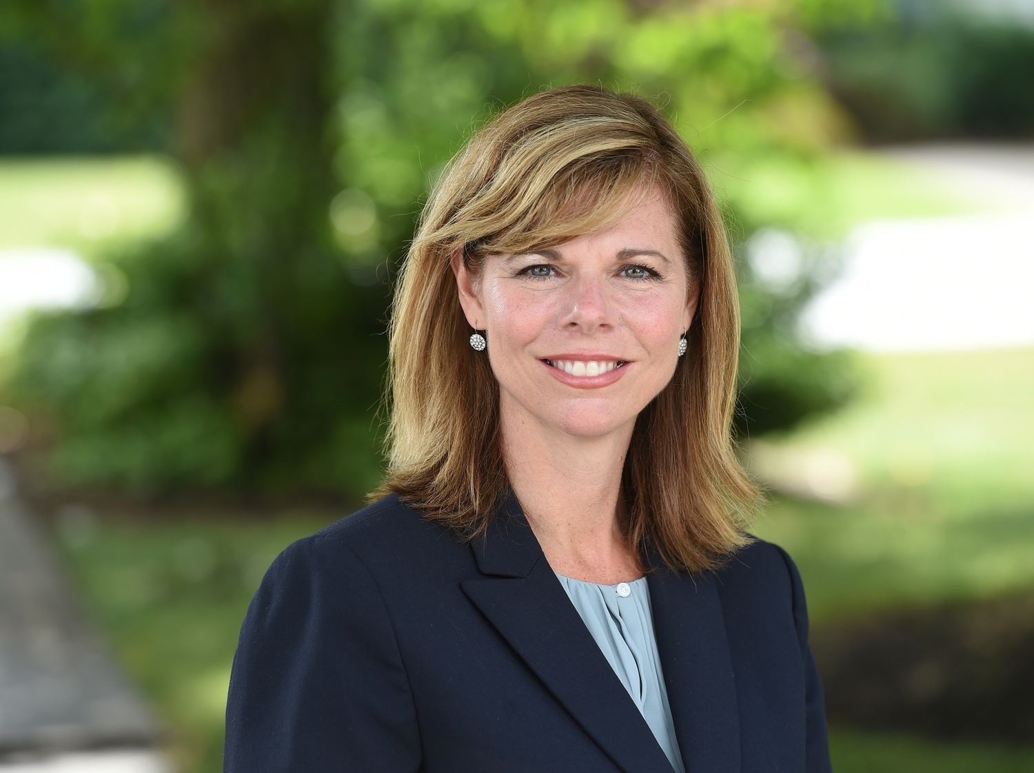Smiling woman with shoulder-length blonde hair wearing a navy blazer outdoors