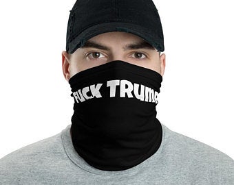 Person wearing a black face mask and dark cap; “TRUMP” is visible on the mask.