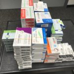 Assorted boxed medicines and treatment kits arranged in stacks on a dark surface.