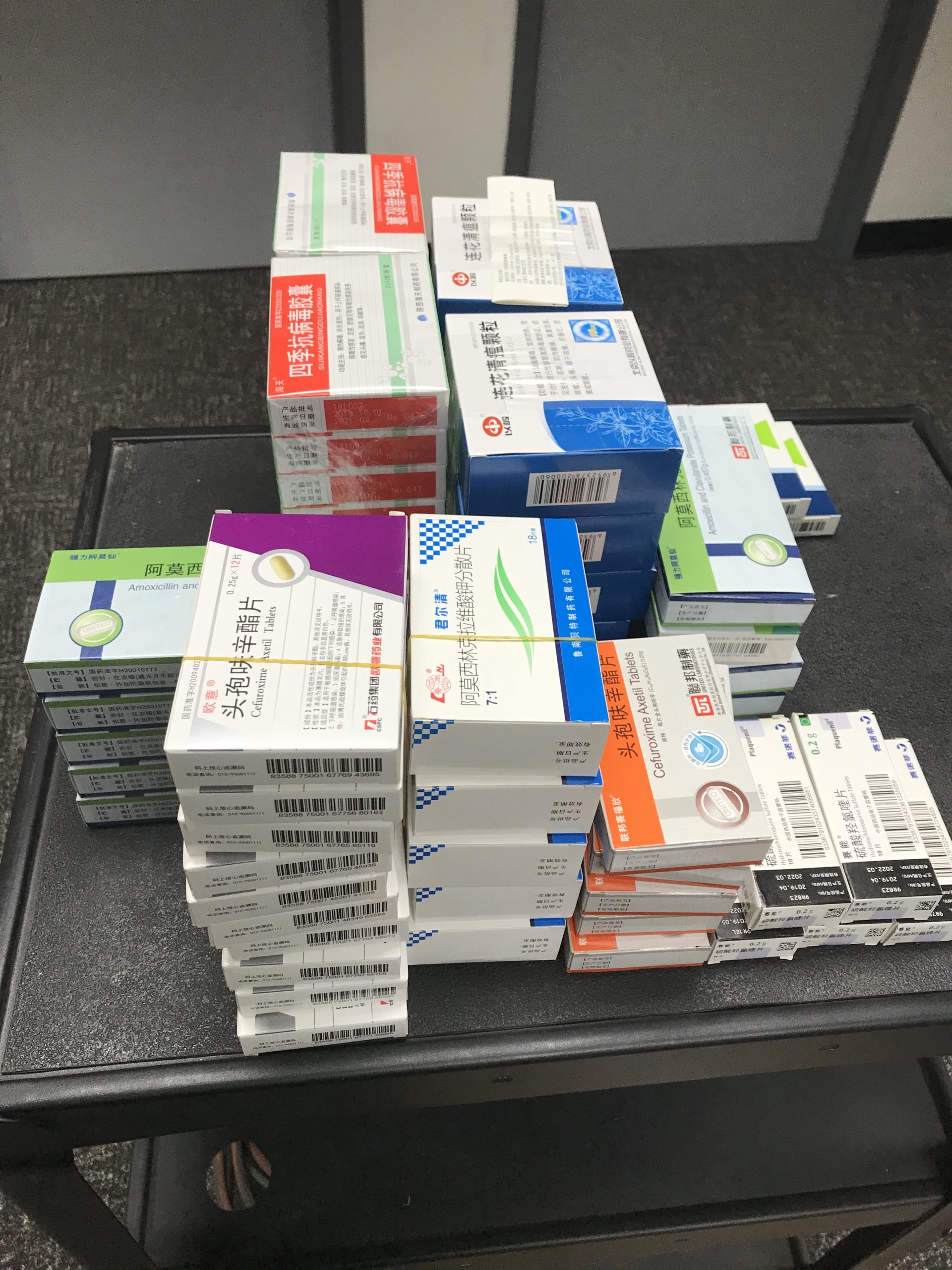 Assorted boxed medicines and treatment kits arranged in stacks on a dark surface.