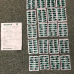 Dozens of blister-pack pills and a labeled envelope laid on a gray surface.