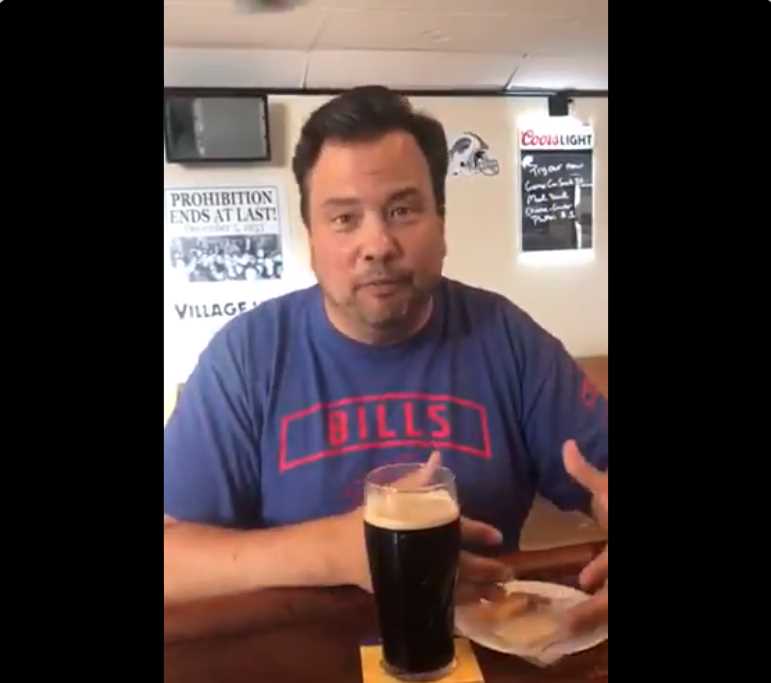 Man seated at a bar holding his hand near a pint glass