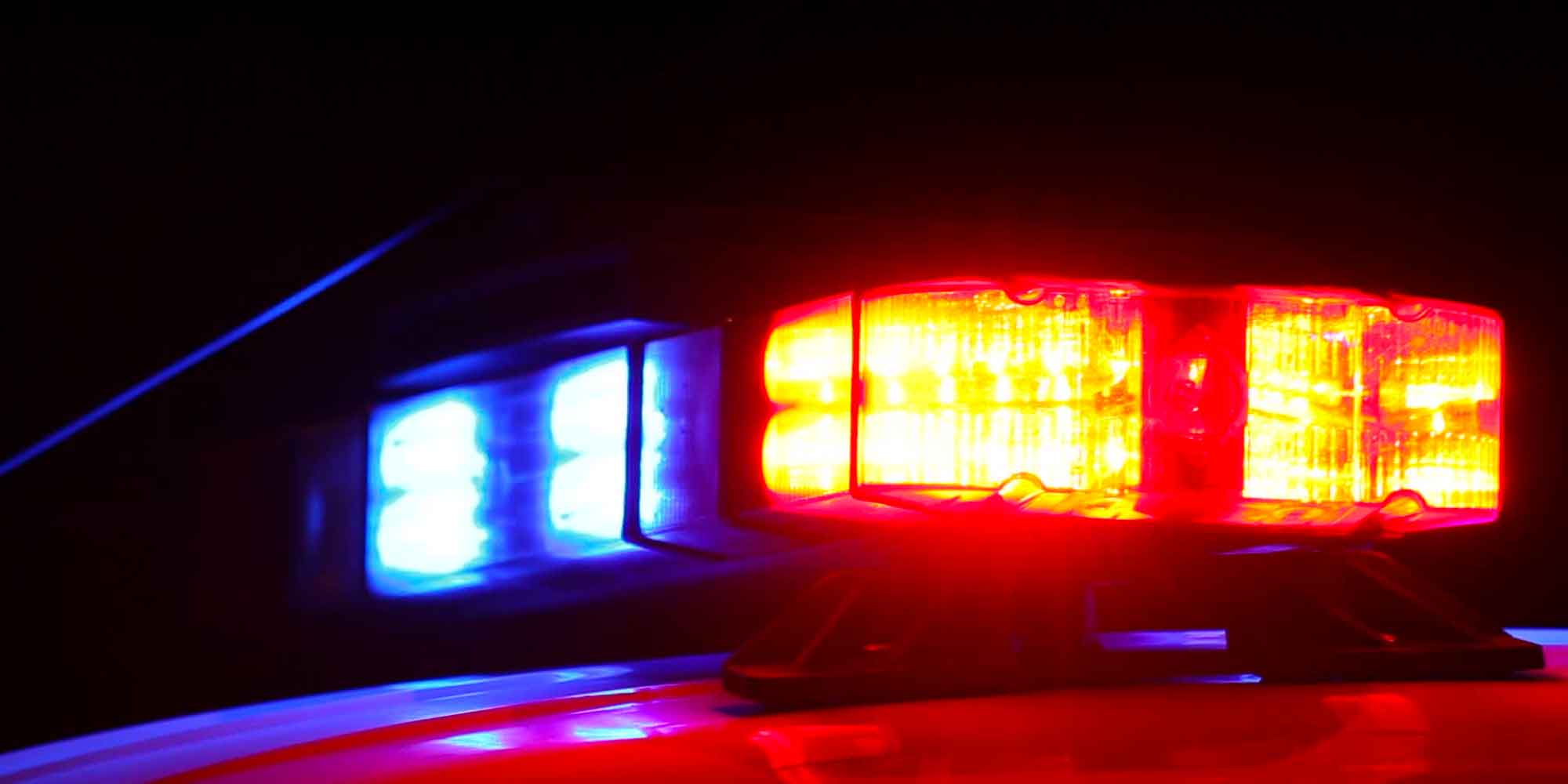Red and blue emergency lights flash from a police vehicle at night.
