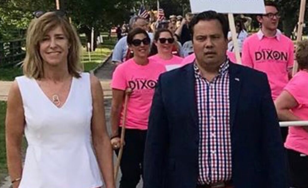 Man and woman stand in front of a crowd wearing bright pink T-shirts outdoors.