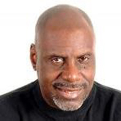 Close-up headshot of a bald man against a plain light background.