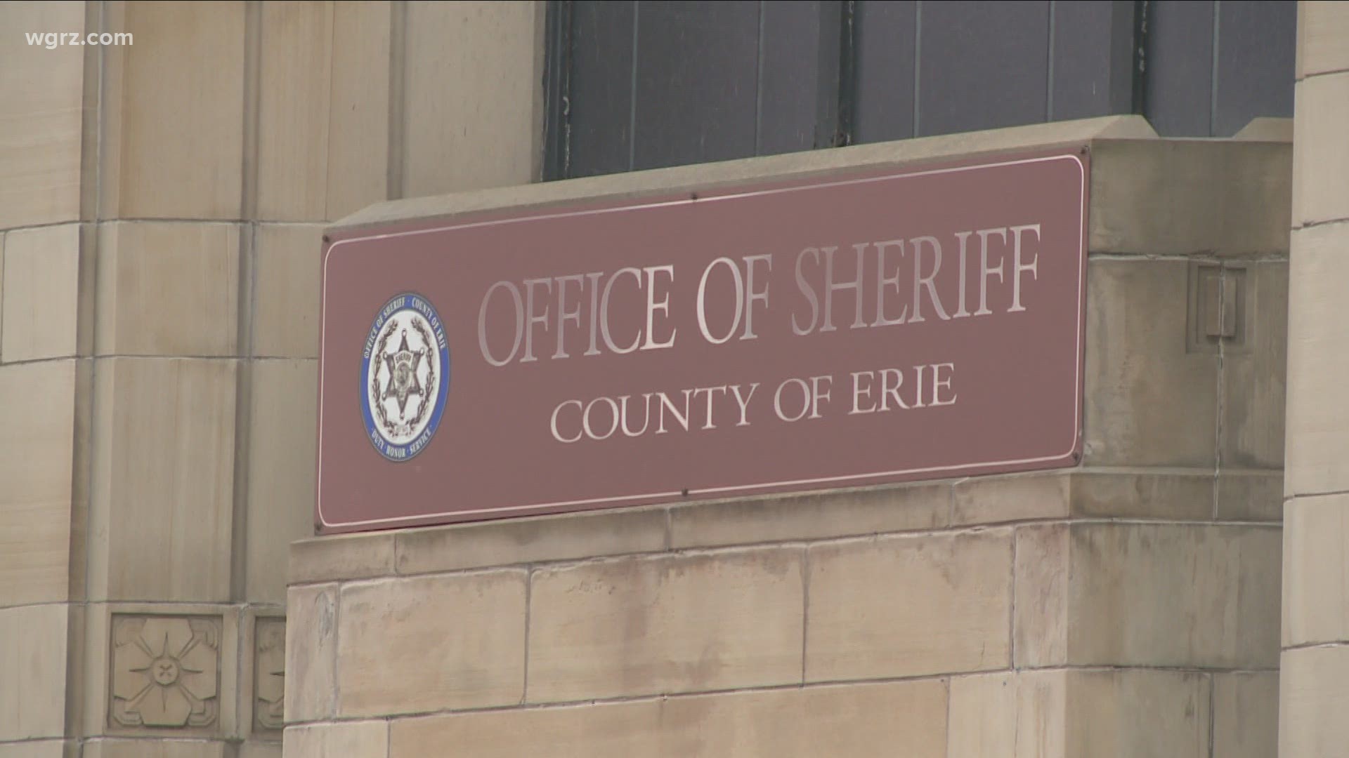 Maroon sign reading “Office of Sheriff, County of Erie” mounted on stone wall.