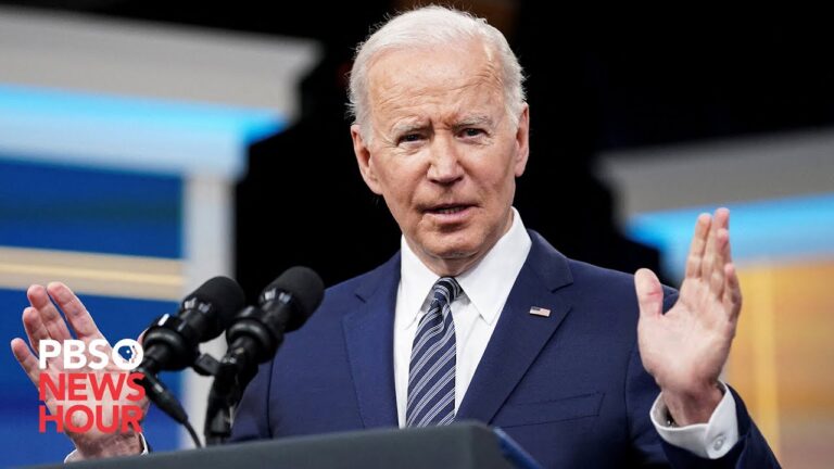 President Biden gestures with both hands while speaking at a podium with microphones.