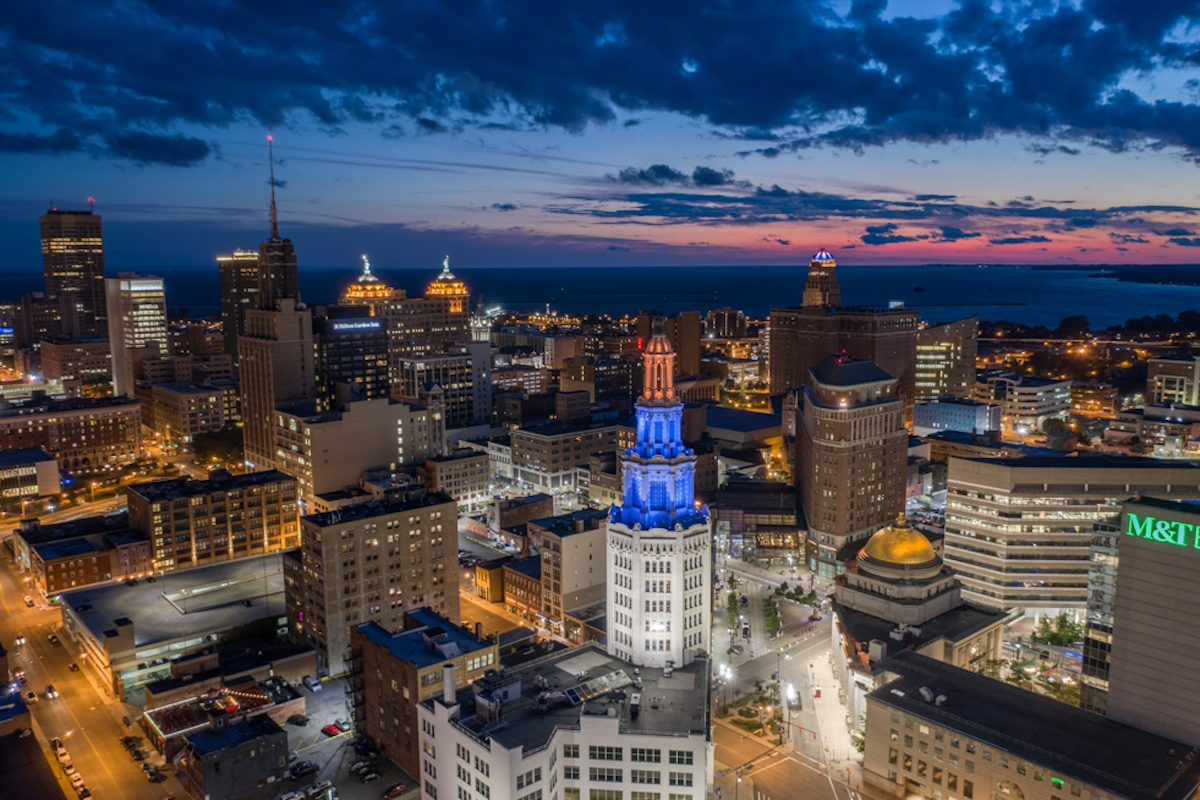 Downtown skyline at dusk with illuminated buildings and a church dome in blue light.