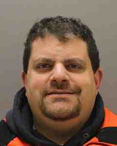Man with short dark hair and facial hair wearing a dark hoodie with orange trim
