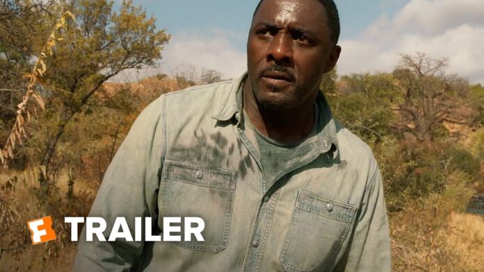 Man in a denim jacket stands outdoors among trees and dry grass.