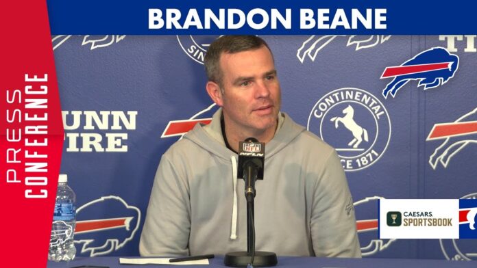 Brandon Beane speaks at a podium during a press event with Buffalo Bills logos behind him.