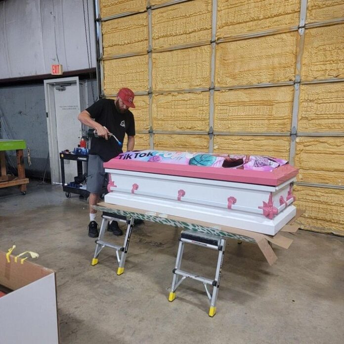 Person assembling a long decorated display on wheeled stands near a building wall.