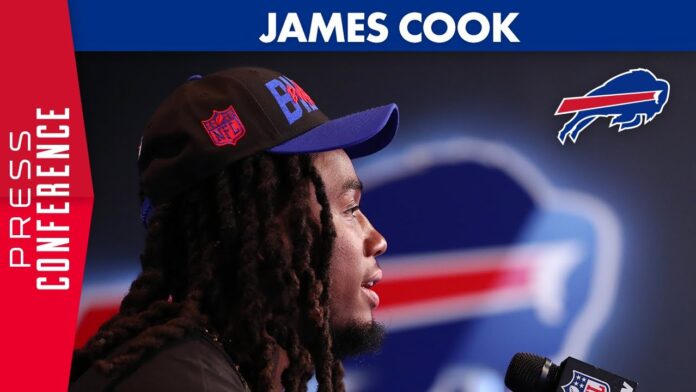 James Cook wearing a black Bills cap speaks into a microphone against a Bills backdrop