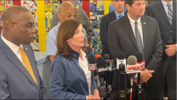 Woman and men in suits stand at microphones during a press remarks event