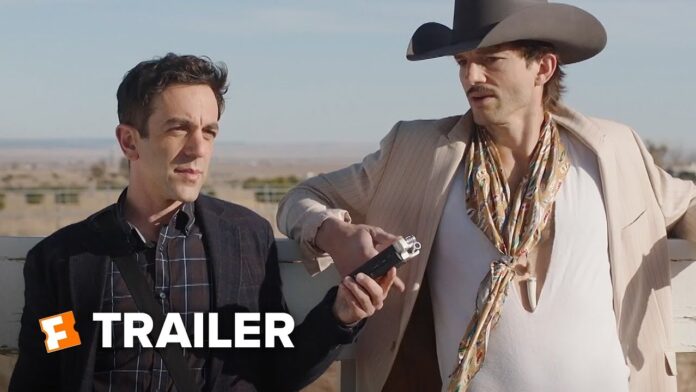 Two men in suits and a cowboy hat, one holding a camera-like device, outdoors.