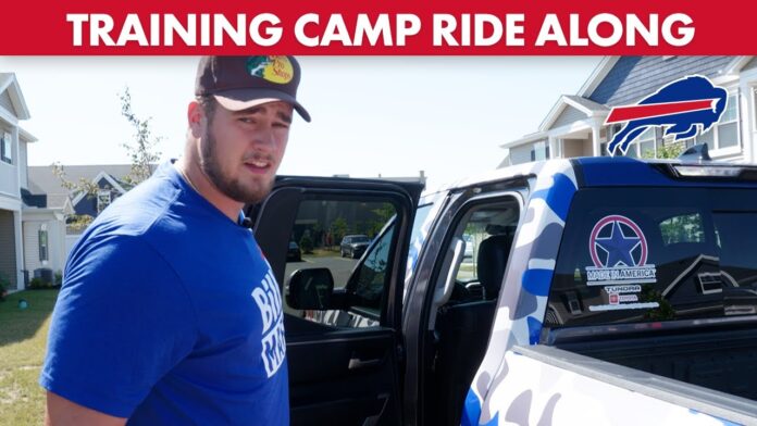 Man in blue shirt and cap stands beside a Toyota Tundra with football logo on door.