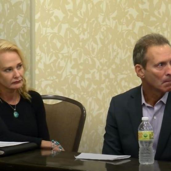 Two people sit at a meeting table with papers and a bottled water in front.