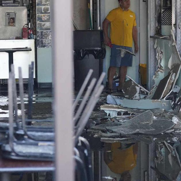 Worker in yellow shirt stands amid debris inside a damaged doorway
