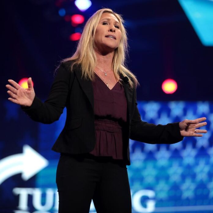 Blonde woman in dark blazer and pants gestures with both hands on stage