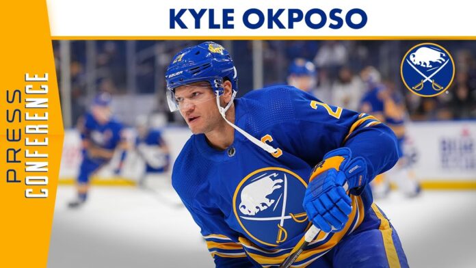 Male hockey player in blue Buffalo Sabres jersey holding a stick on the ice