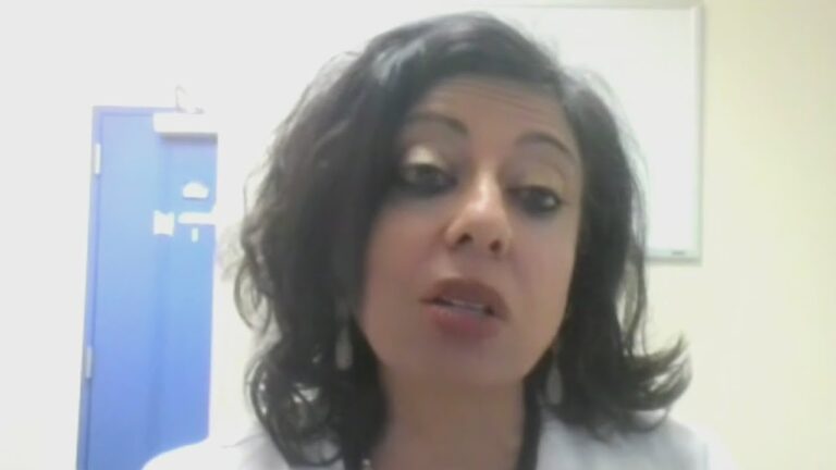 Woman speaking on camera indoors with medical room background