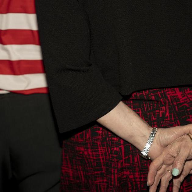 Two people’s hands clasped; one wears a bracelet and ring; an American flag is nearby.