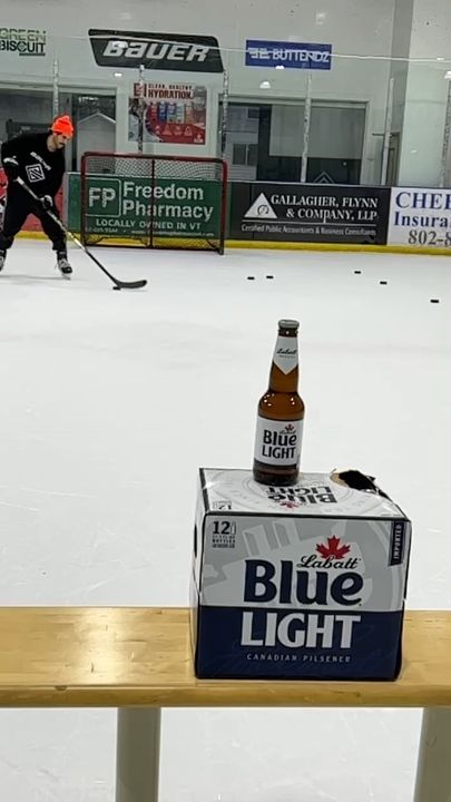Beer bottle and Blue Light box sit on an indoor hockey bench; players practice nearby.