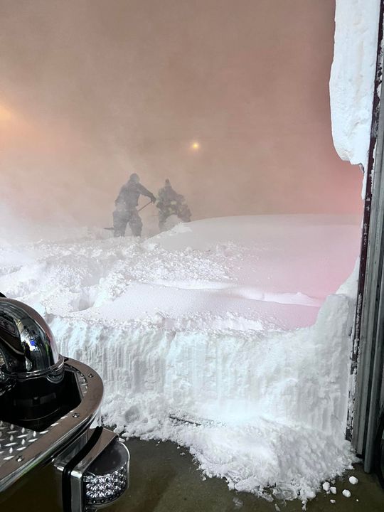Two people in dark clothing move through deep snow beside a vehicle door.
