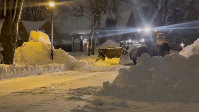 Snow plow truck working on a dim street at night with headlights on.