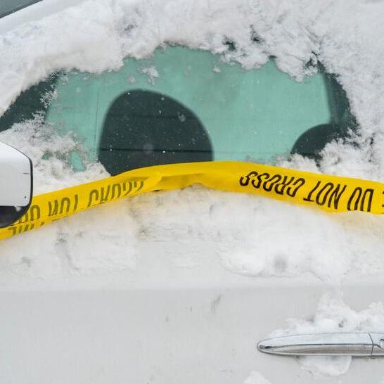 Yellow caution tape stretches across snowy ground near the front of a vehicle.