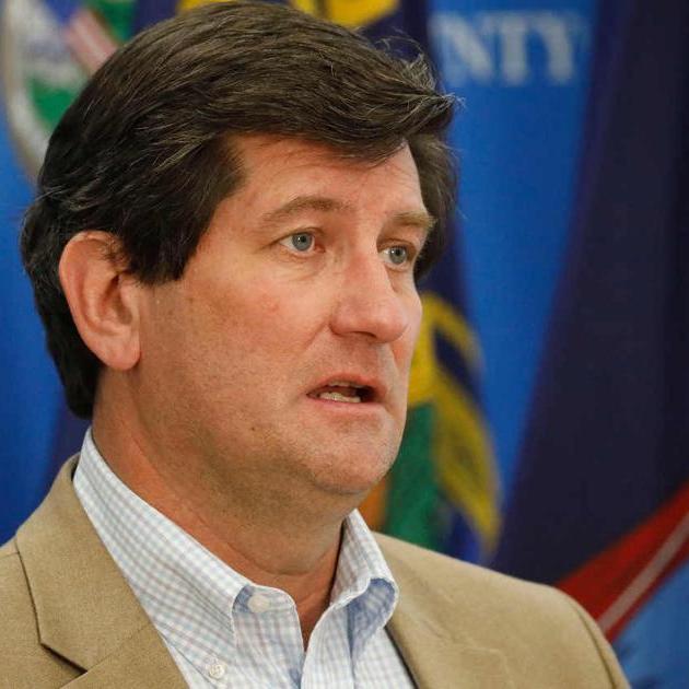 A man speaking with flags in the background.