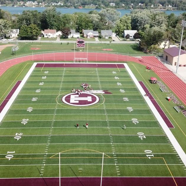 Aerial view of a green football field with red track and an E logo at midfield