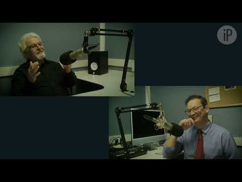 Two people wearing head mics in a podcast radio booth with recording equipment