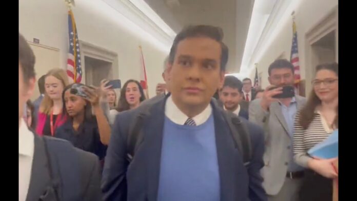 Man in suit walks through hallway as people behind him take photos and videos