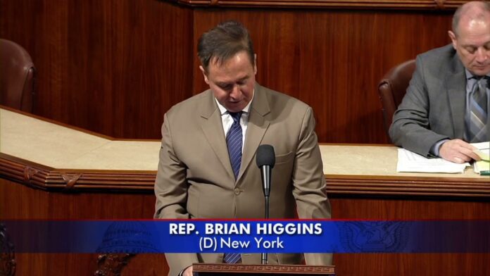 Lawmaker in a beige suit reads from notes at a podium with microphone.