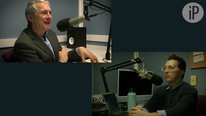 Two people sit at a radio podcast studio with microphones and recording equipment